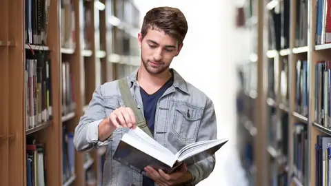 Mlody chłopak z ksiązką w bibliotece